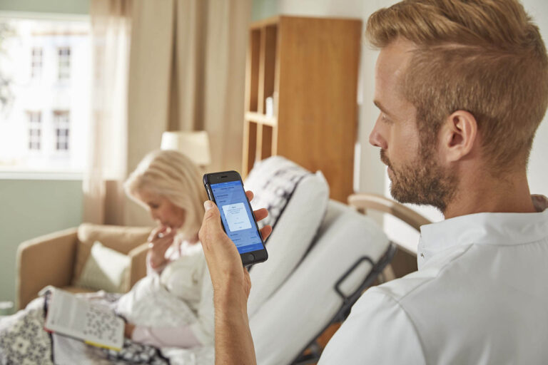 Pfleger kontrolliert auf seinem Handy die Daten seiner Patientin