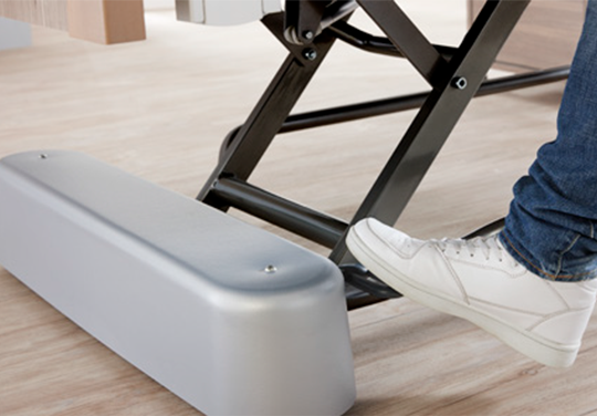 Fuß betätigt die Bremse des Pflegebetts, daneben sieht man die Rollenabdeckung