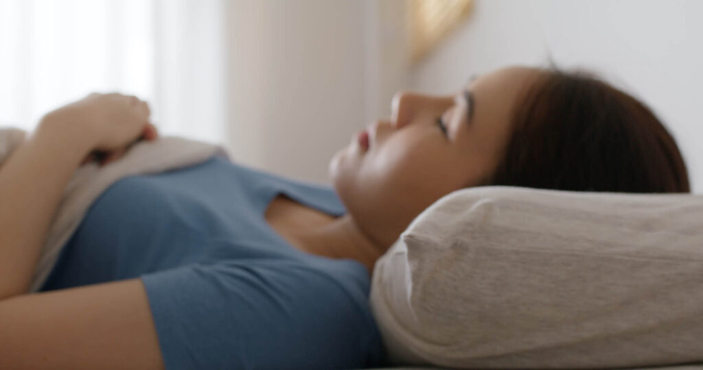 Frau liegt im Bett auf einem Nackenkissen