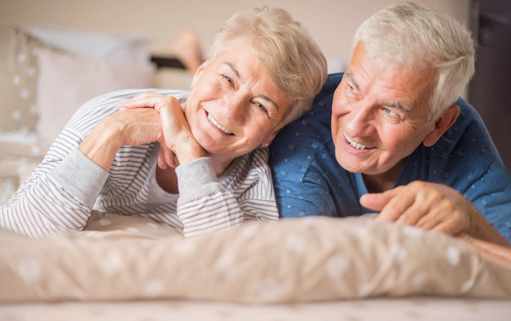 Älteres lachendes Paar liegt zusammen auf dem Bauch im Bett
